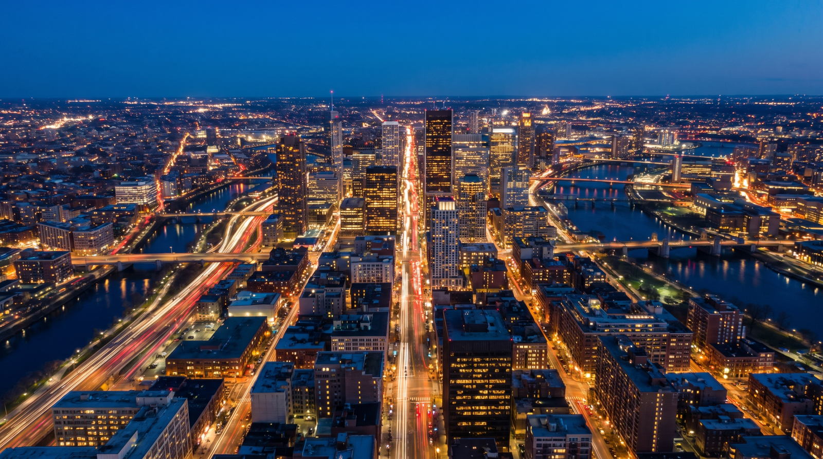 Foto aerea noturna de uma cidade iluminada com trilhas de luz nas avenidas na blue hour