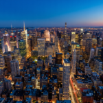Foto aerea noturna de uma cidade iluminada com trilhas de luz no ceu azul da blue hour