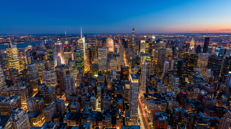 Foto aerea noturna de uma cidade iluminada com trilhas de luz no ceu azul da blue hour