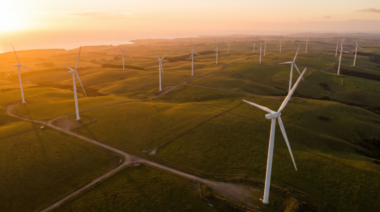 Vista aerea de um parque eolico com turbinas brancas em colinas verdes ao entardecer