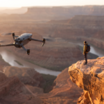 Drone DJI-style orbitando uma pessoa num penhasco ao entardecer, tomada cinematografica automatica