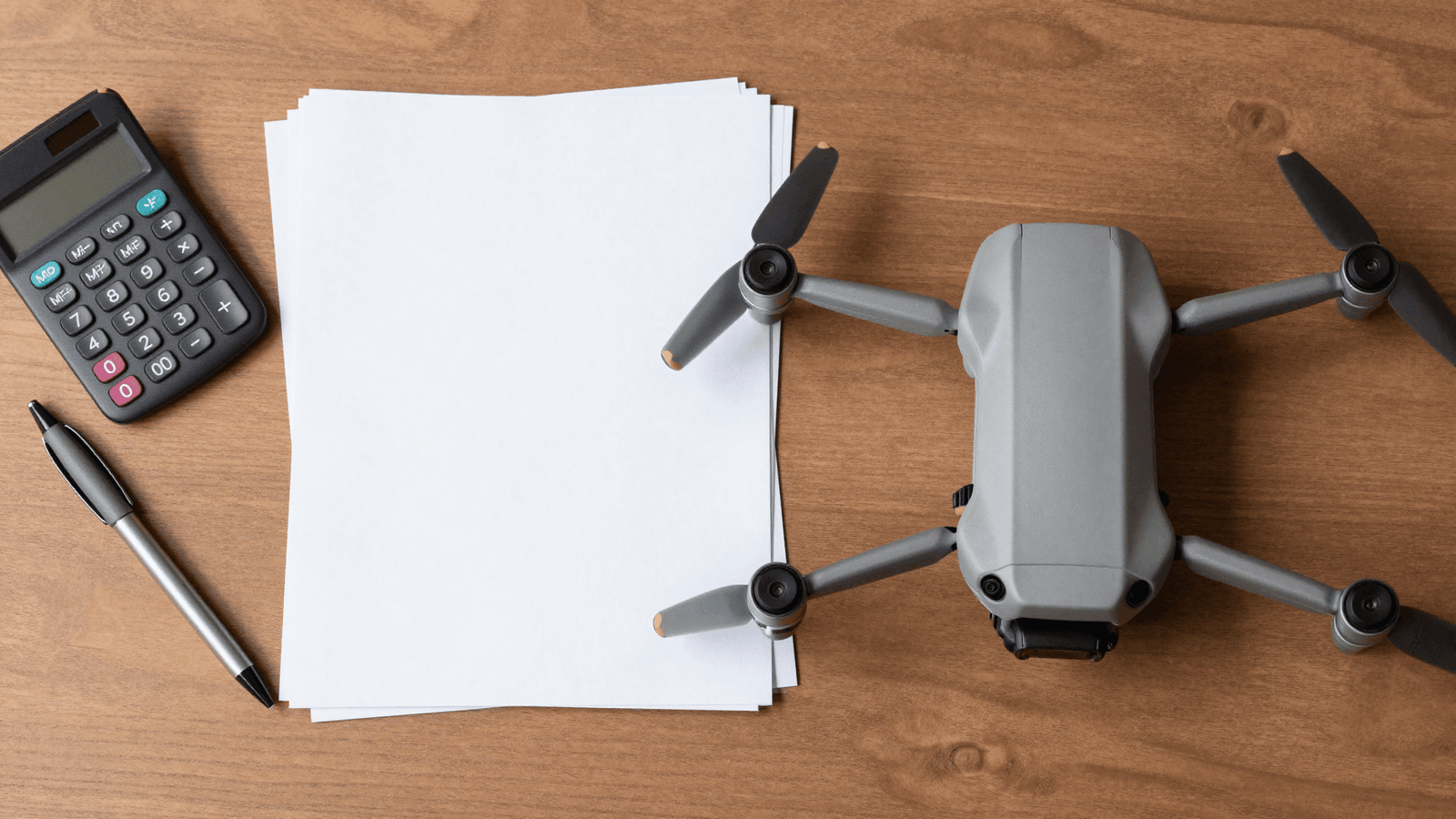 Calculadora, papéis e drone dobrado sobre a mesa, representando a contabilidade do piloto