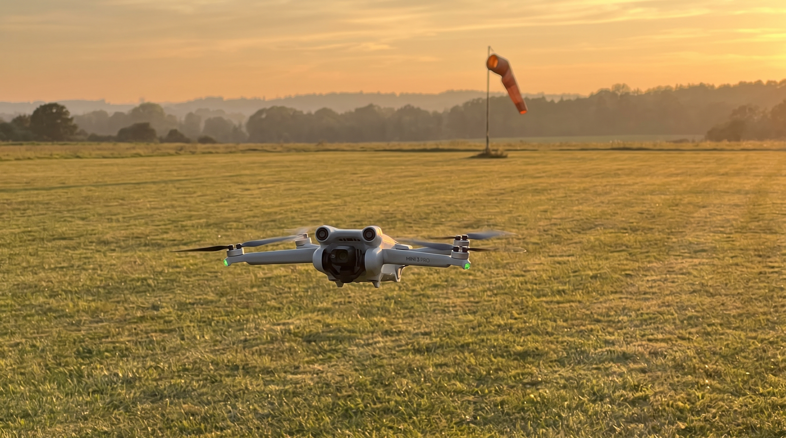 Drone leve voando baixo em um campo de aeromodelismo ao entardecer, longe de pessoas