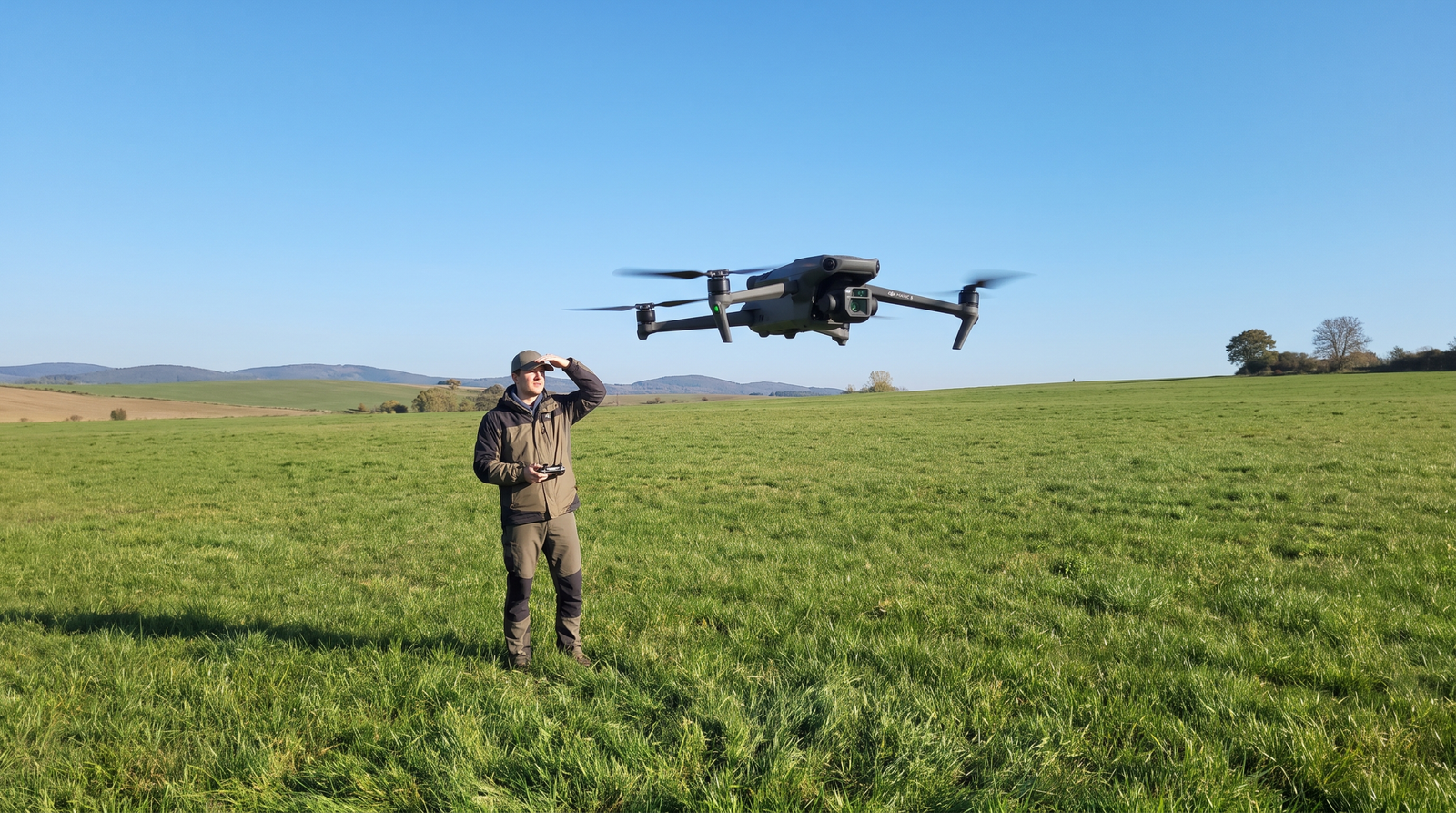 Drone DJI-style pairando baixo sobre um gramado com a pessoa mantendo a linha de visada