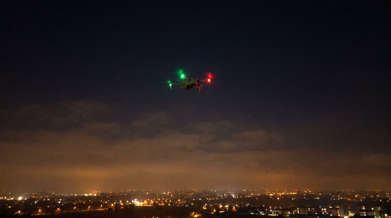Drone com LEDs verde e vermelho piscando no ceu noturno, mostrando como reconhecer um drone a noite