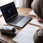 Pessoa estudando com notebook e drone dobrado sobre a mesa