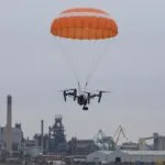Drone profissional descendo suspenso por um paraquedas aberto