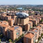 Drone de carga sobrevoando area residencial urbana no Brasil com caixa de entrega presa embaixo