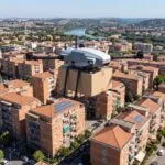 Drone de carga sobrevoando area residencial urbana no Brasil com caixa de entrega presa embaixo