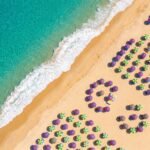 Foto aerea top-down de praia com mar turquesa, areia dourada e guarda-sois coloridos em padroes graficos
