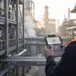 Tecnico com controle de drone em area industrial