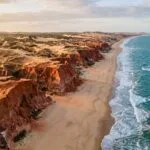 Vista aerea das falesias avermelhadas e da praia larga de Canoa Quebrada
