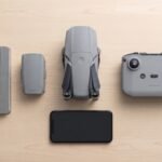 Drone dobrado, controle, celular e bateria organizados sobre uma mesa de madeira