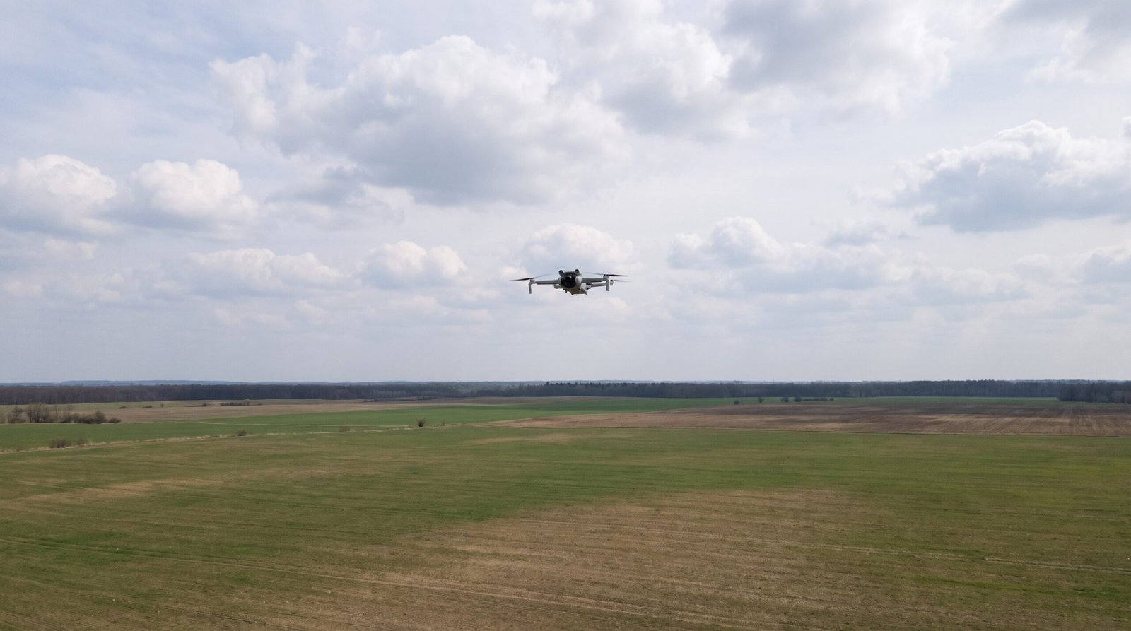 Drone pequeno cruza o céu aberto sobre área rural, longe de pessoas
