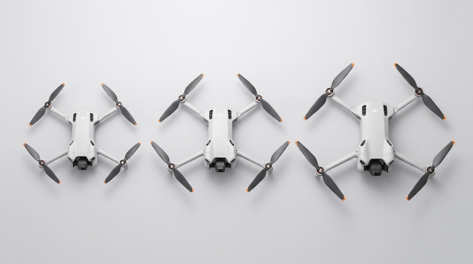 Três drones de tamanhos diferentes enfileirados sobre superfície clara