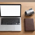Mesa vista de cima com laptop, planilha em branco e um drone pequeno