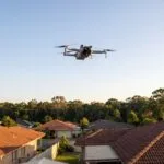 Drone pequeno visto do quintal, alto no céu sobre os telhados das casas