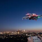 Drone pairando ao anoitecer com as luzes acesas sobre a silhueta de uma cidade
