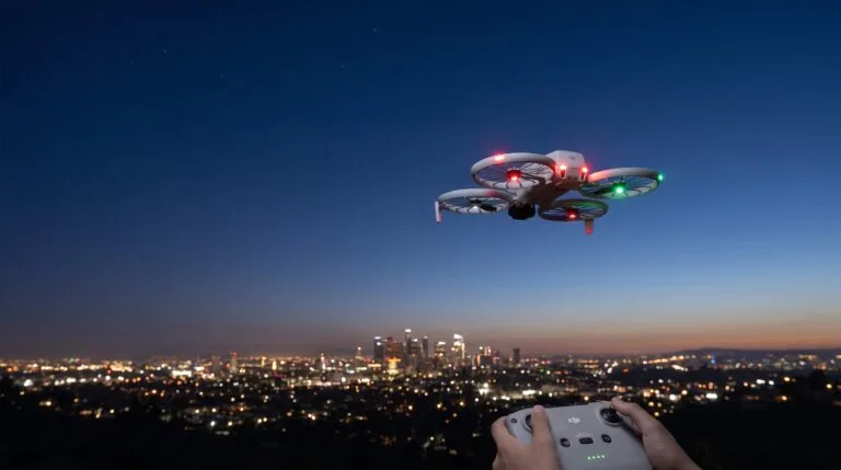 Drone pairando ao anoitecer com as luzes acesas sobre a silhueta de uma cidade