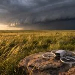 Drone pousado em campo aberto com nuvens escuras de tempestade se aproximando
