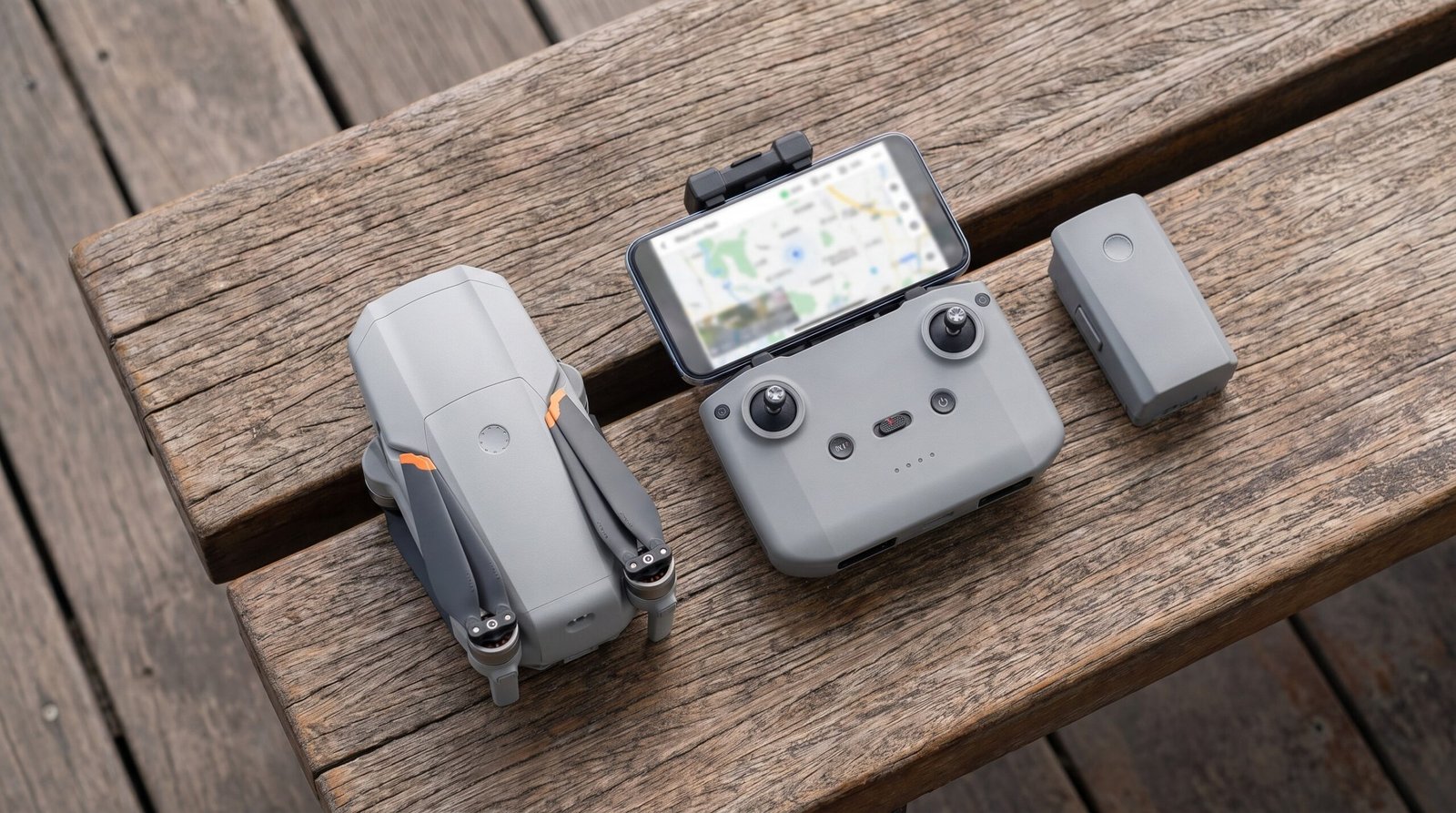 Drone dobrado, controle com celular e bateria sobre um banco