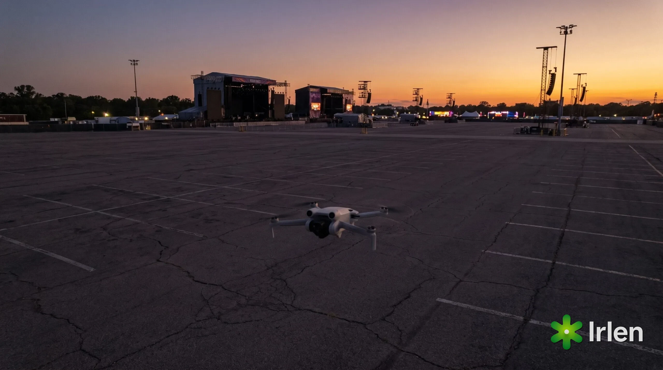 Drone pequeno pairando sobre uma área vazia, com as estruturas de um festival ao longe