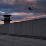 Drone paira alto sobre o muro de concreto de uma unidade prisional ao entardecer