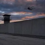 Drone paira alto sobre o muro de concreto de uma unidade prisional ao entardecer