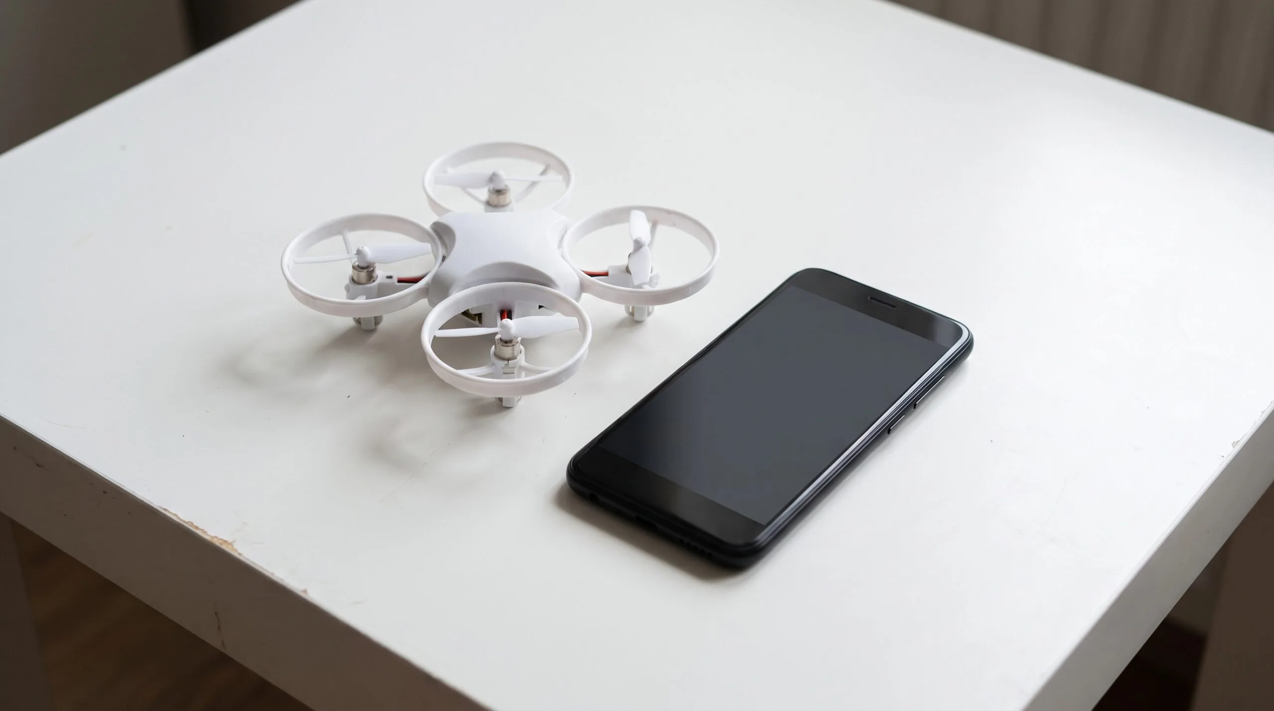 Quadricóptero branco de plástico ao lado de um celular sobre a mesa