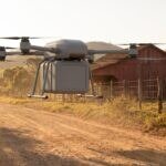 Drone de carga pairando sobre a estrada de uma fazenda com uma caixa acoplada