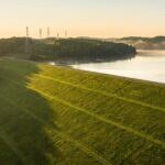 Barragem de terra com talude gramado e reservatório ao fundo