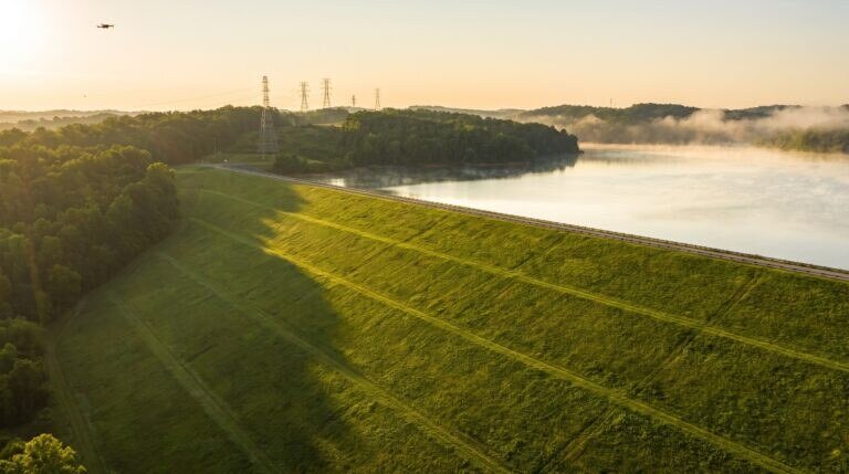 Barragem de terra com talude gramado e reservatório ao fundo