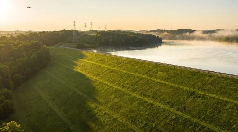 Barragem de terra com talude gramado e reservatório ao fundo