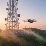 Torre de telecom com antenas e drone pairando ao lado ao amanhecer