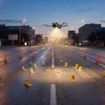 Cena de reconstituição de acidente com marcadores e drone pairando ao anoitecer