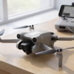 Drone pequeno sobre a mesa com uma etiqueta branca na fuselagem e o controle ao fundo