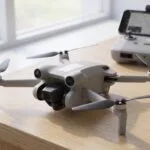 Drone pequeno sobre a mesa com uma etiqueta branca na fuselagem e o controle ao fundo