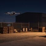 Drone pairando à noite sobre pátio industrial iluminado