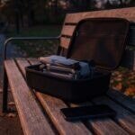 Drone DJI Air 3S usado dentro de um case aberto sobre um banco de praça ao entardecer