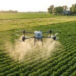 Drone agrícola DJI Agras T50 pulverizando soja com uma casa de fazenda ao fundo, longe da área aplicada