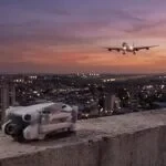 Drone compacto da linha DJI Mini dobrado num terraço ao entardecer, com um avião pousando ao longe
