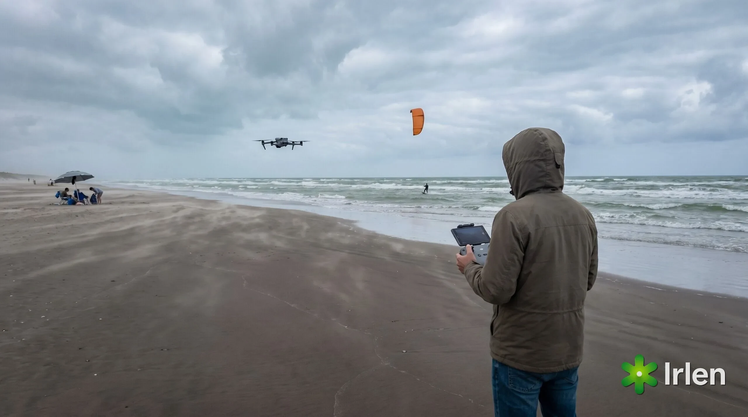 Piloto de costas na areia com controle DJI RC 2 filmando um kitesurfista ao longe, com banhistas distantes