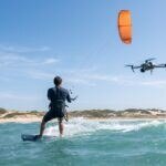 Drone DJI Air 3S filmando um kitesurfista de costas no mar azul-turquesa
