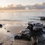 Drone DJI Mini 4 Pro pousado numa pedra na beira de uma praia ao nascer do sol
