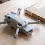 Drone DJI Mini 4 Pro com a bateria puxada para fora do compartimento, ao lado da caixa