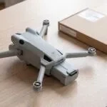 Drone DJI Mini 4 Pro com a bateria puxada para fora do compartimento, ao lado da caixa