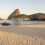 Drone DJI Avata 2 pairando baixo sobre a areia da Praia do Flamengo, com o Pão de Açúcar ao fundo