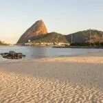Drone DJI Avata 2 pairando baixo sobre a areia da Praia do Flamengo, com o Pão de Açúcar ao fundo