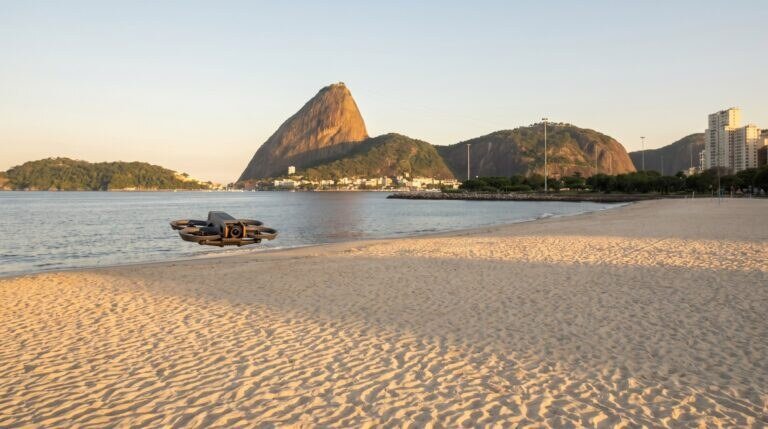 Drone DJI Avata 2 pairando baixo sobre a areia da Praia do Flamengo, com o Pão de Açúcar ao fundo