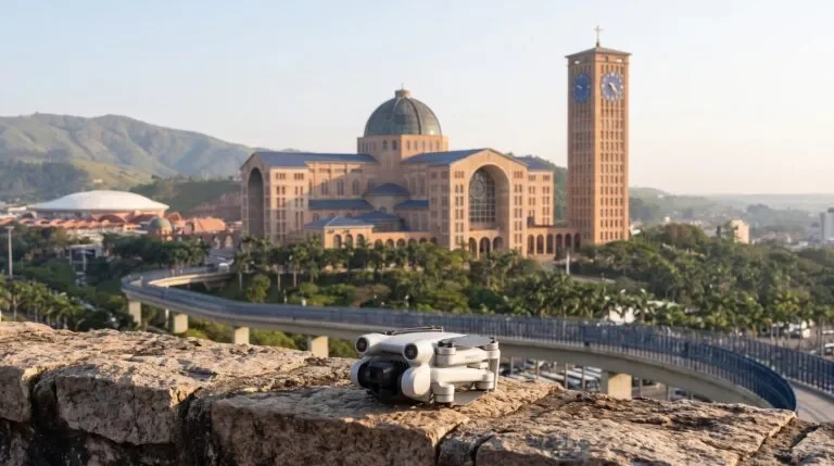 Drone DJI Mini 4 Pro dobrado sobre um muro de pedra, com a Basílica do Santuário Nacional de Aparecida e a torre ao fundo